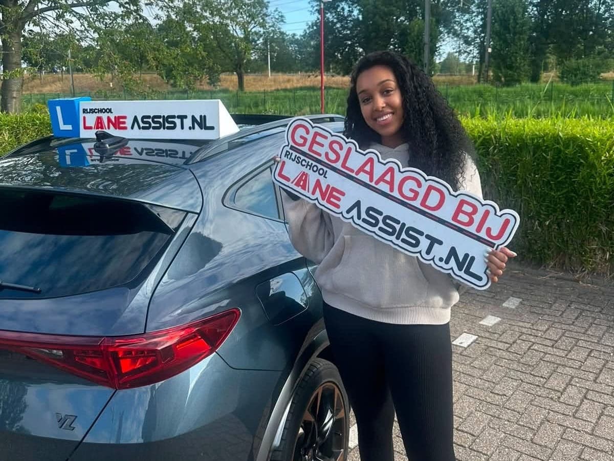 Geslaagde leerling met het Lane Assist bord bij de automaat-lesauto