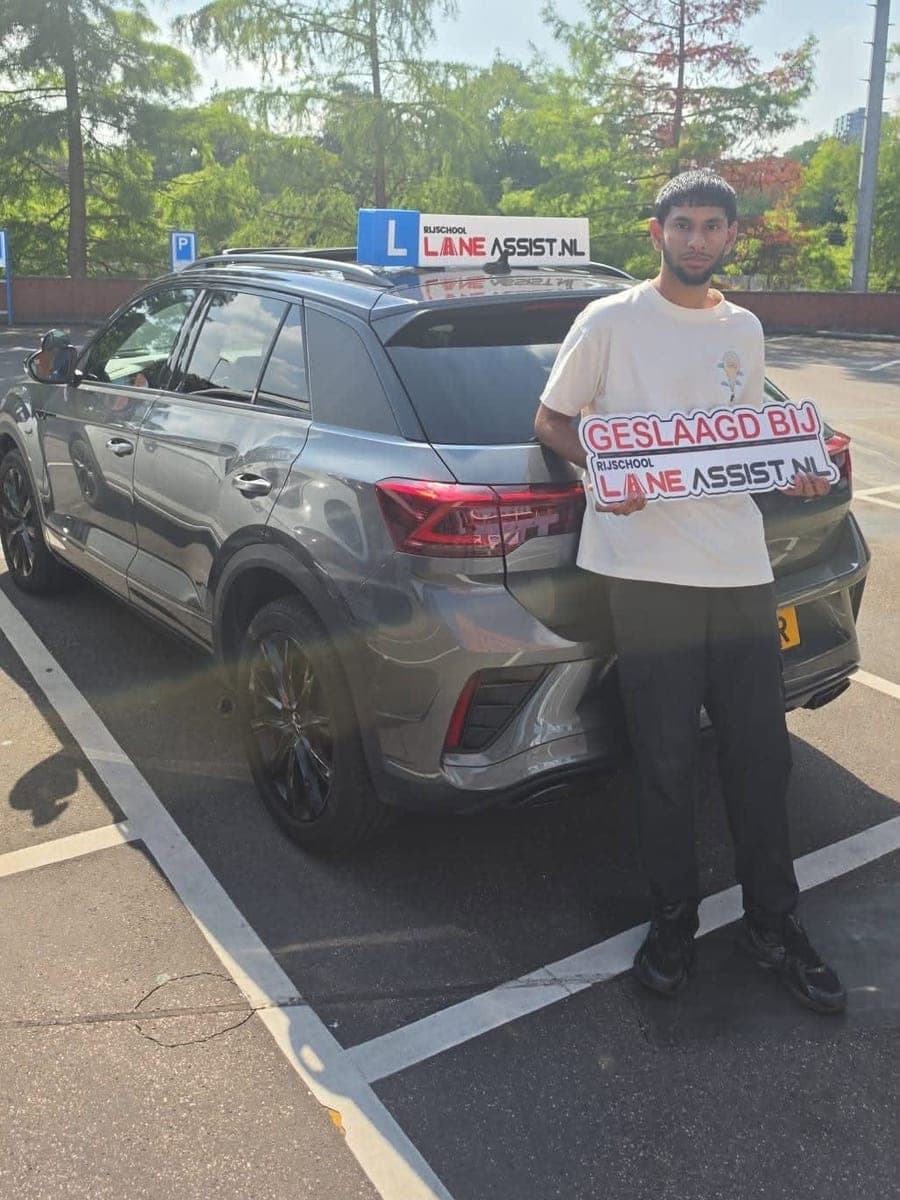 Geslaagde leerling met het Lane Assist bord naast de lesauto